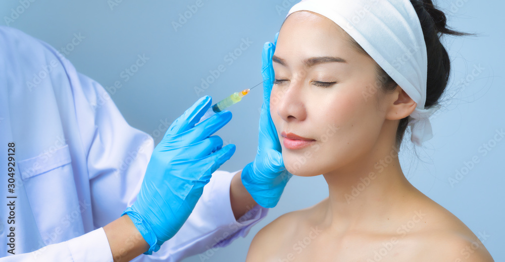 Naklejka premium Asian young woman gets injection in her lips. Woman in beauty salon. plastic surgery clinic.Beautiful woman gets injection in her face.