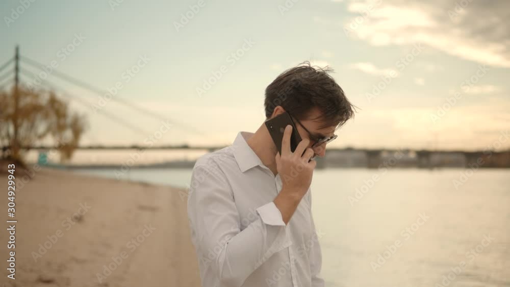 Handsome Man Talking By Smartphone Among Pond And Looking To Distance.Businessman At River Beach Using Mobile Phone And Enjoying Sunset.Beautiful Attractive Man Talking On Mobile Phone With Friend. Handsome Man Talking By Smartphone Among Pond And Looking To Distance.Businessman At River Beach Using Mobile Phone And Enjoying Sunset.Beautiful Attractive Man Talking On Mobile Phone With Friend.