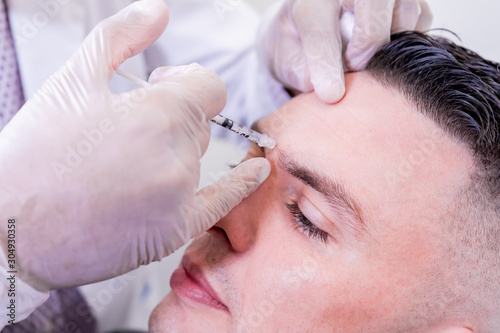 Caucasian man undergoing beauty spa botulinum neurotoxin Botox treatment for anti-aging  to smooth wrinkles as a cometic solution. Injecting forehead to relax muscles with a non-invasive procedure.
