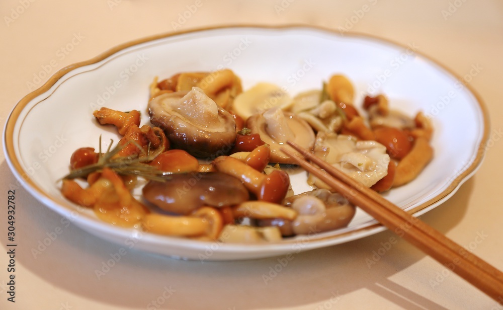 Mushrooms are small salty in sauce wet on a plate of white and sticks for eating Mushrooms are small salty in sauce wet on a plate of white and sticks for eating