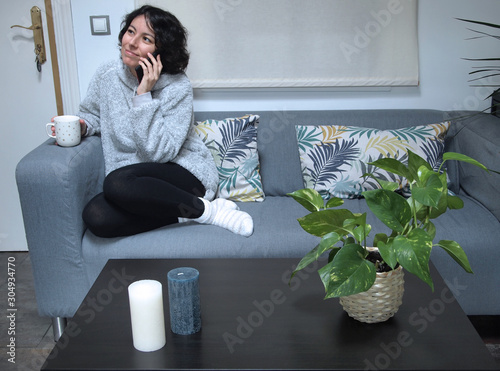 Φωτογραφία Young caucasian woman talking on her phone and drinking coffee in pajamas, sitti