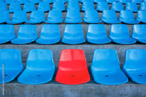 Single or one red seat or bench in the middle or center of blue chair in the football or soccer stadium.