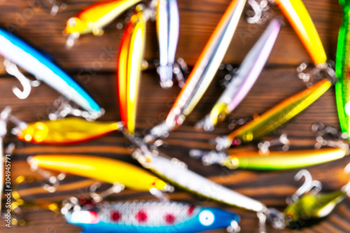 Blurred background with fishing tackle. Defocused fishing tackles and wobbler on wooden board. Fishing hooks, lures and baits. Blurry fishing gear on a dark table