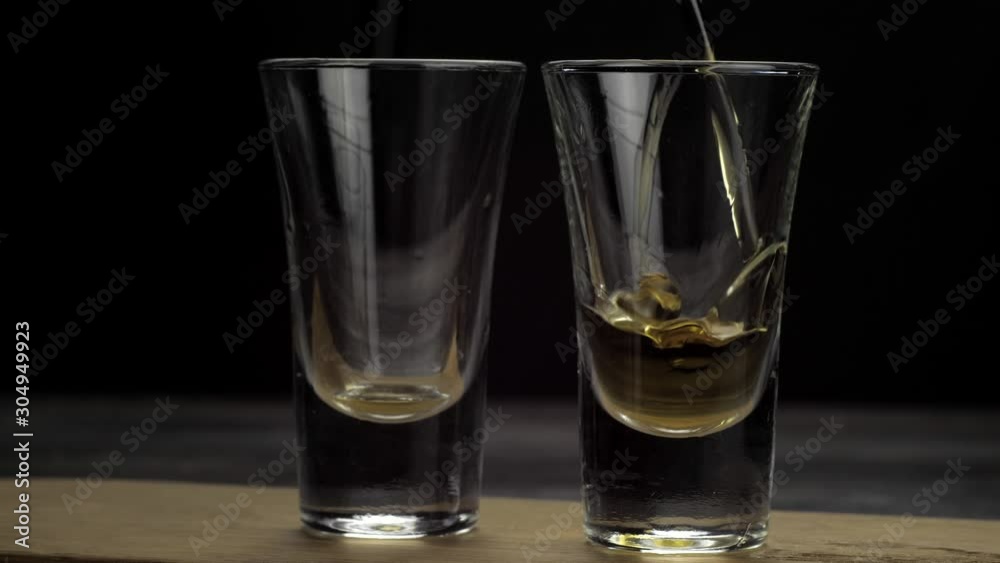 tequila is poured into two glasses on black background