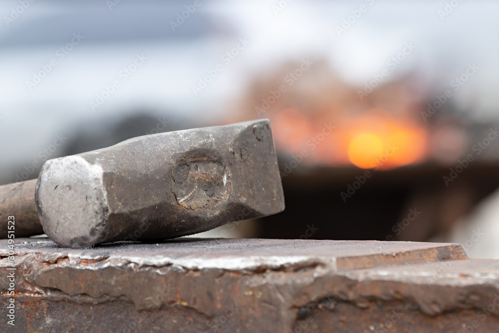 Old rusty hammer lies on the anvil with flame of brazier forge on background. Blacksmith, metalsmith, farrier tools. Close view. Old rusty hammer lies on the anvil with flame of brazier forge on background. Blacksmith, metalsmith, farrier tools. Close view.