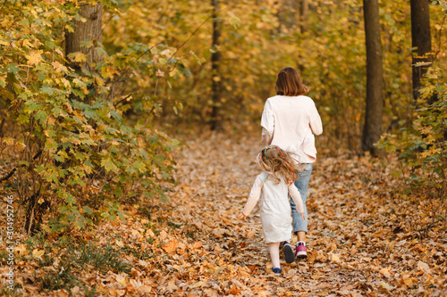Mother and her little daughter running and having fun in the autumn park photographed from the back © Maksym