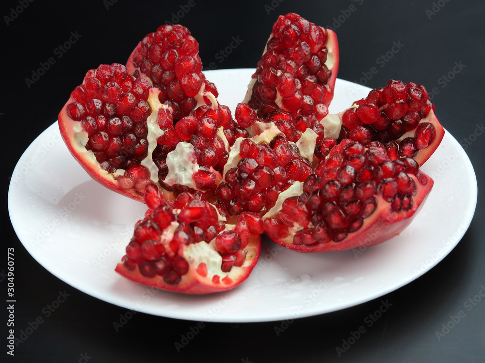 Ripe pomegranate in a white plate on a dark background Ripe pomegranate in a white plate on a dark background