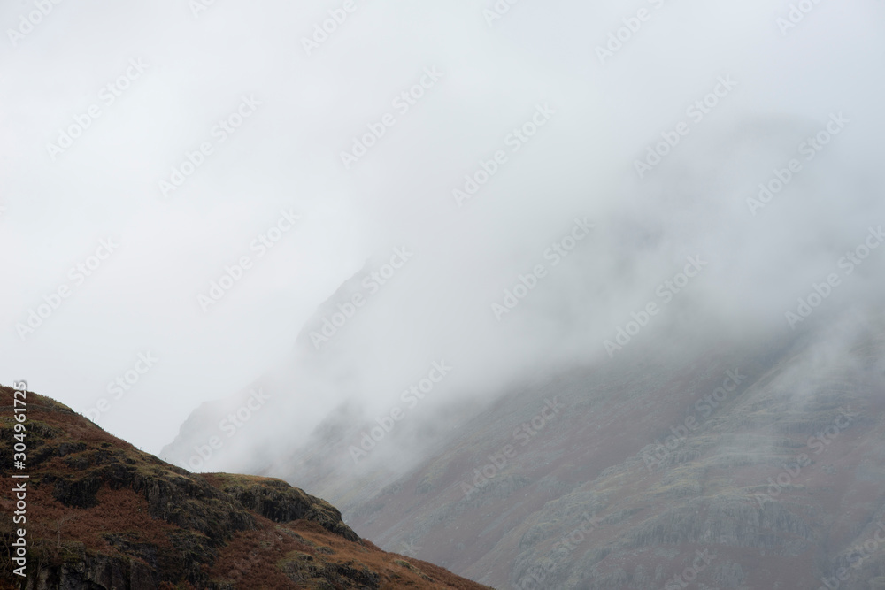 Beautiful Autumn Fall landscape image of Langdale Pikes mountain range in Lake District in mist and low cloud