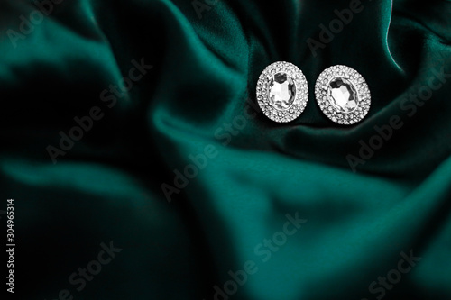 Luxury diamond earrings on dark emerald green silk, holiday glamour jewelery present photo