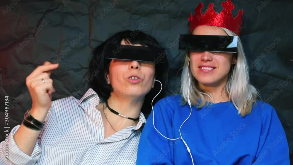 Two lesbians at a bachelorette party listening to music with headphones.