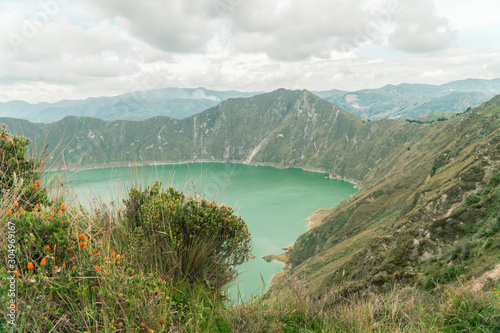 Volcano crater lake view, Quilotoa. Dramatic perspective of Quilotoa lake and volcano crater, with view of mountains, hiking path trail loop and cloudy sky from viewpoint. Shot in Ecuador. Green blue