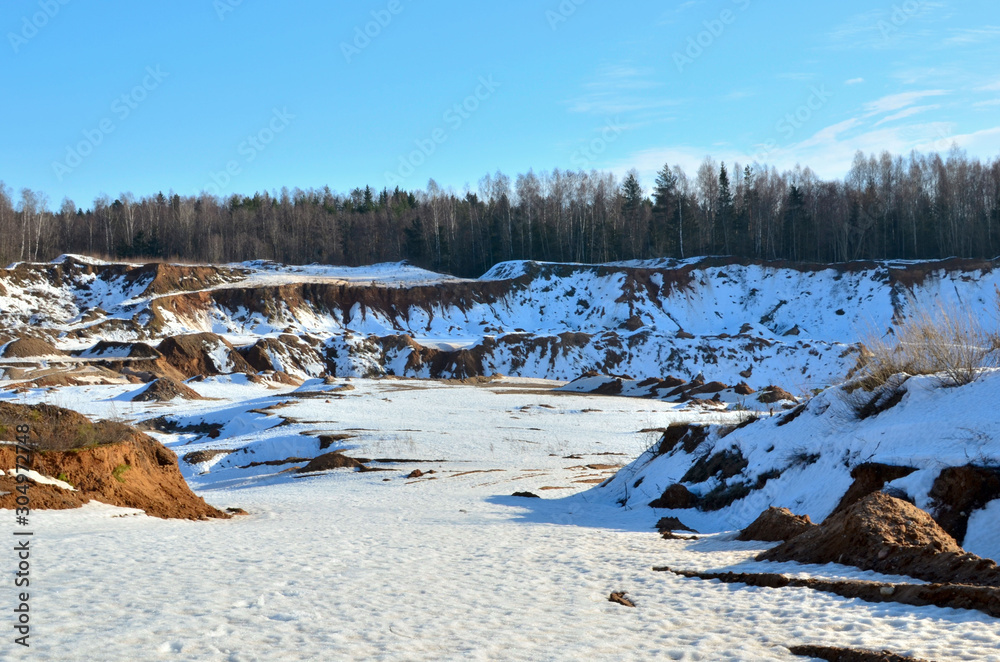 Fototapeta premium View from the mountain to the red sand in the snow of a small canyon in the Minsk region, Radoshkovichi, the village of Praleski, mining quarry.