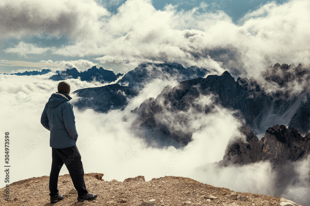 Man standing on the edge of view point with Dolomite Alps covered with clouds, Tre Cime di Lavaredo park