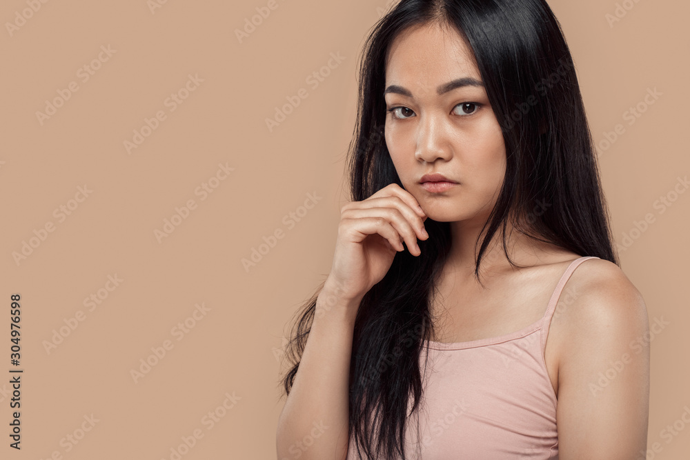 Freestyle. Asian girl in top standing isolated on grey touching face looking camera curious Freestyle. Asian girl in top standing isolated on grey touching face looking camera curious
