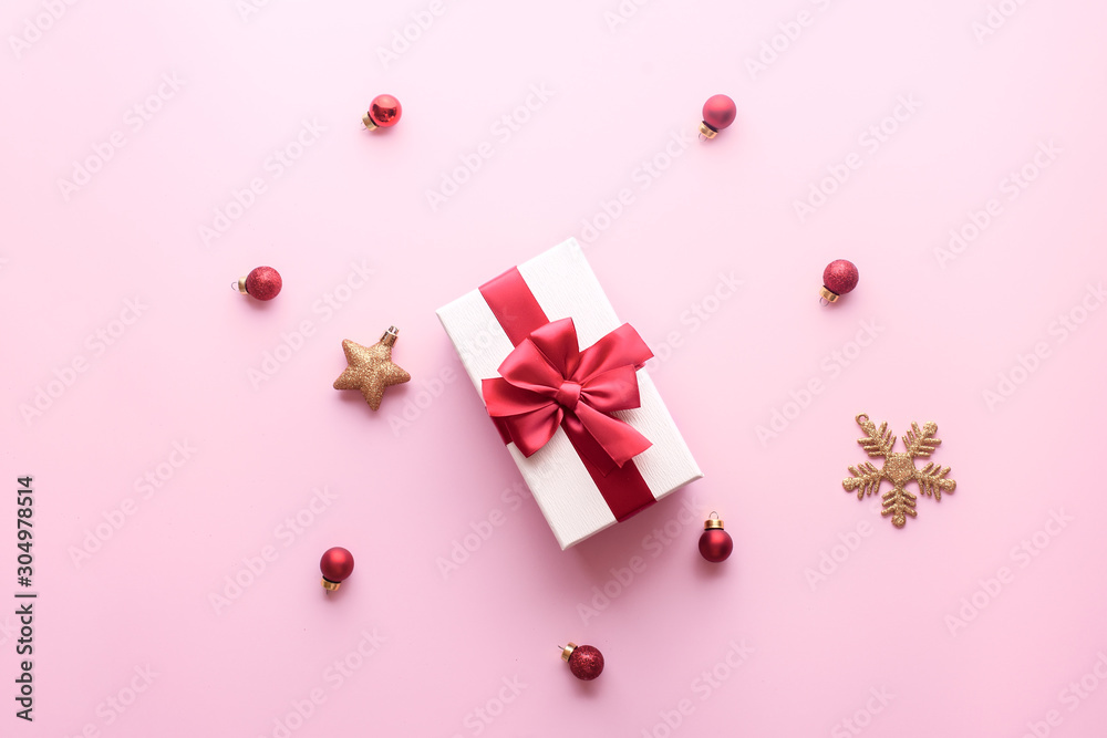 christmas gift box with red ribbon on a pastel pink background with red christmas tree toys, golden stars and cones. Holidays, New Year 2020 present concept. Trendy colors,Top view, flat lay.