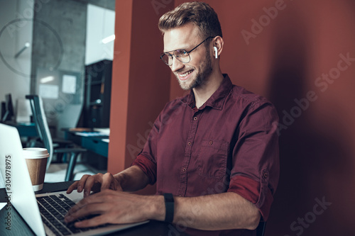 Happy young man is sitting with laptop near wall