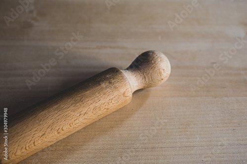 Rolling pin resting on a wooden board, with flour specks. Manual kneading process for homemade bakery.