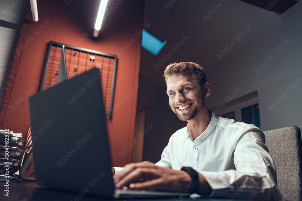 Smiling male employee sitting late at work Smiling male employee sitting late at work
