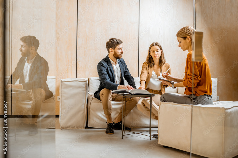 © rh2010 - Young couple talking with a sales manager or real estate agent, sitting on the comfortable couch in the office