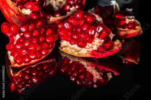 Fresh organic slices of pomegranate with reflection on shiny black background
