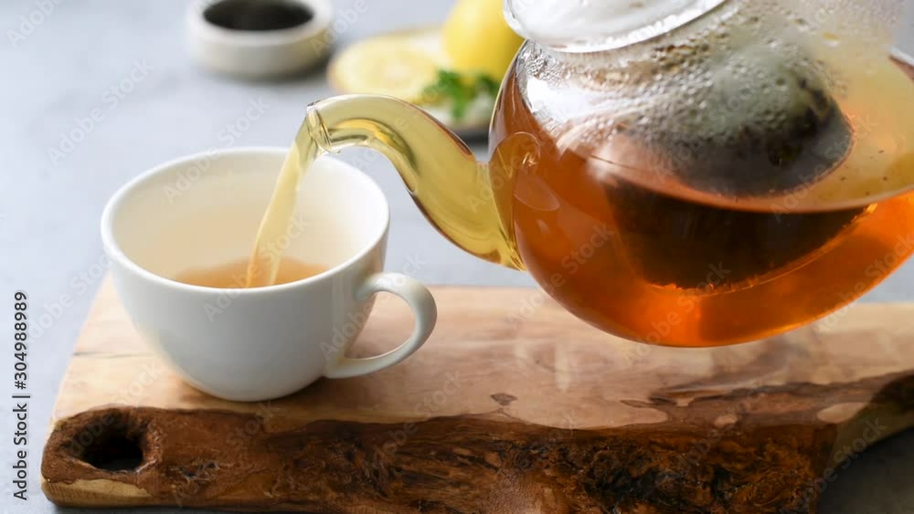 Pouring tea in cup. Brewed black tea in glass tea pot. Hot beverage chinese tea