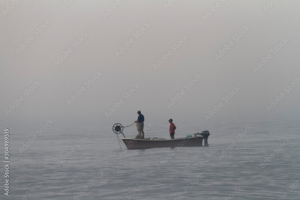 Naklejka premium Fishermen on the boat in foggy morning, Long Beach in Ulcinj in Montenegro