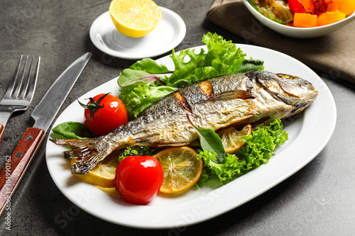 Delicious roasted fish with lemon and vegetables on dark grey table