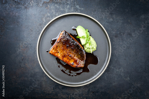 Minimalistic design Japanese salmon fish filet with vegetable and wasabi creme glazed in teriyaki sauce as closeup on a modern design plate
