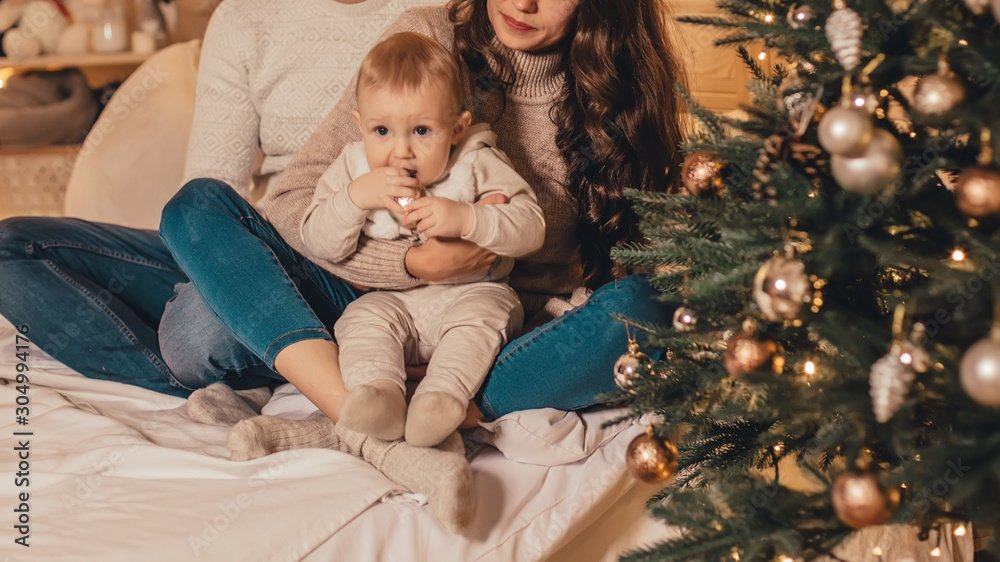 Happy family sitting on bed and celebrating new year near Christmas tree in decorated interior. Celebrating Christmas. Happy family sitting on bed and celebrating new year near Christmas tree in decorated interior. Celebrating Christmas.
