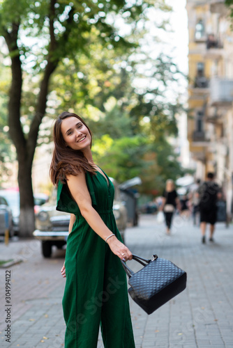 Fashion model wearing green overall posing outdoor. Young beautiful brunette caucasian woman walking summer streets. Beautiful girl, urban portrait.