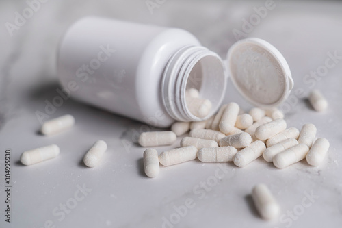 painkillers and drug abuse concept with close up on a bottle of prescription drugs and pill capsules falling out of it on a white marble table