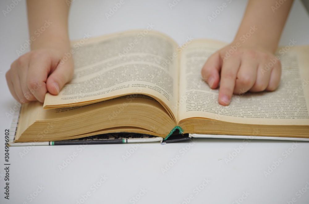Fototapeta premium Little girl reads big book against white background and drives down lines with a finger