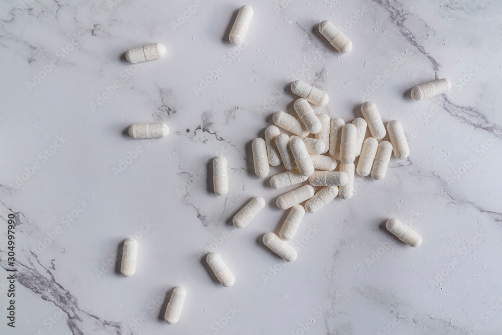 painkillers and drug abuse concept with close up on a bottle of prescription drugs and pill capsules falling out of it on a white marble table painkillers and drug abuse concept with close up on a bottle of prescription drugs and pill capsules falling out of it on a white marble table