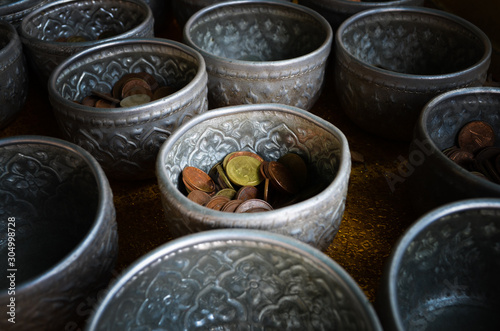 Golden, bronze and silver Thai coins separated in silver bowls for Thai traditional donation at Buddhist temple in Thailand. Coins background texture.