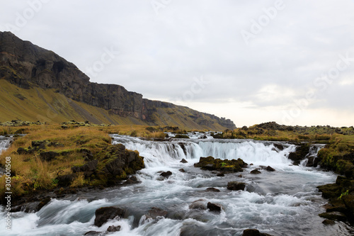 Panoramic summer view of small waterfall near Bjodvegur road. Wonderful sunrise on Iceland, Vik location. Beauty of nature concept background..