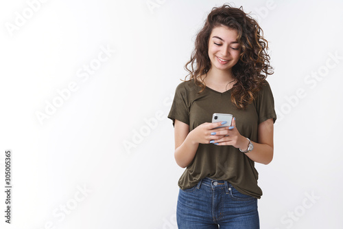 Charming cheerful georgian young curly-haired woman holding smartphone reading message look phone display smiling pleased receive good news via social network, standing white background photo