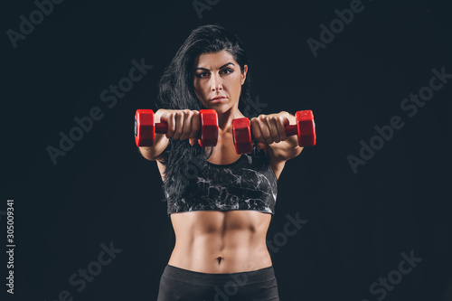 Sporty muscular woman with dumbbells on dark background