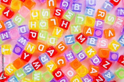 A bunch of little multicolored letters on the surface of a pink background  selective focus