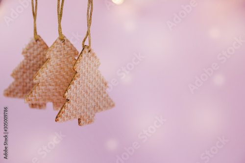 Holiday background, Christmas and new year decorations wooden Christmas trees hanging on a rope on pink background, luminous bokeh, selective focus