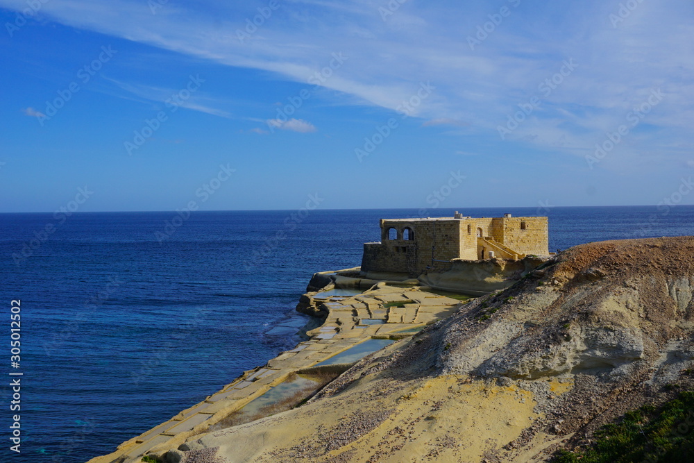 Rocks at the sea, blue sky with small clouds, natural rock formation, beautiful rocky bay in Gozo with abandoned old battery at the background