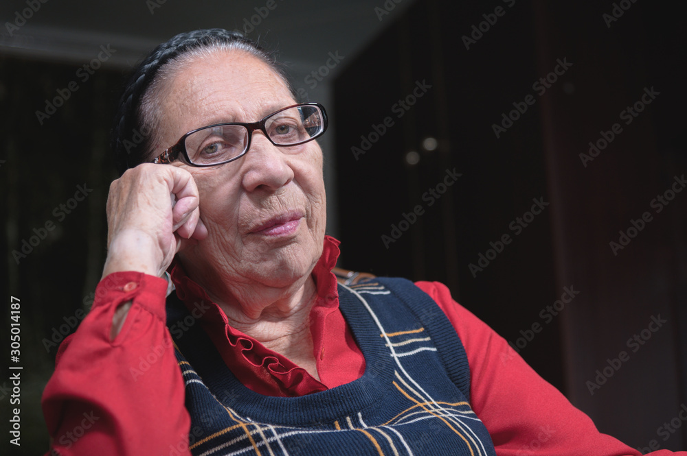 Portrait of an elderly pensive woman in glasses leaning on her arm indoors sitting and thinking. Elderly woman 80 years old Portrait of an elderly pensive woman in glasses leaning on her arm indoors sitting and thinking. Elderly woman 80 years old