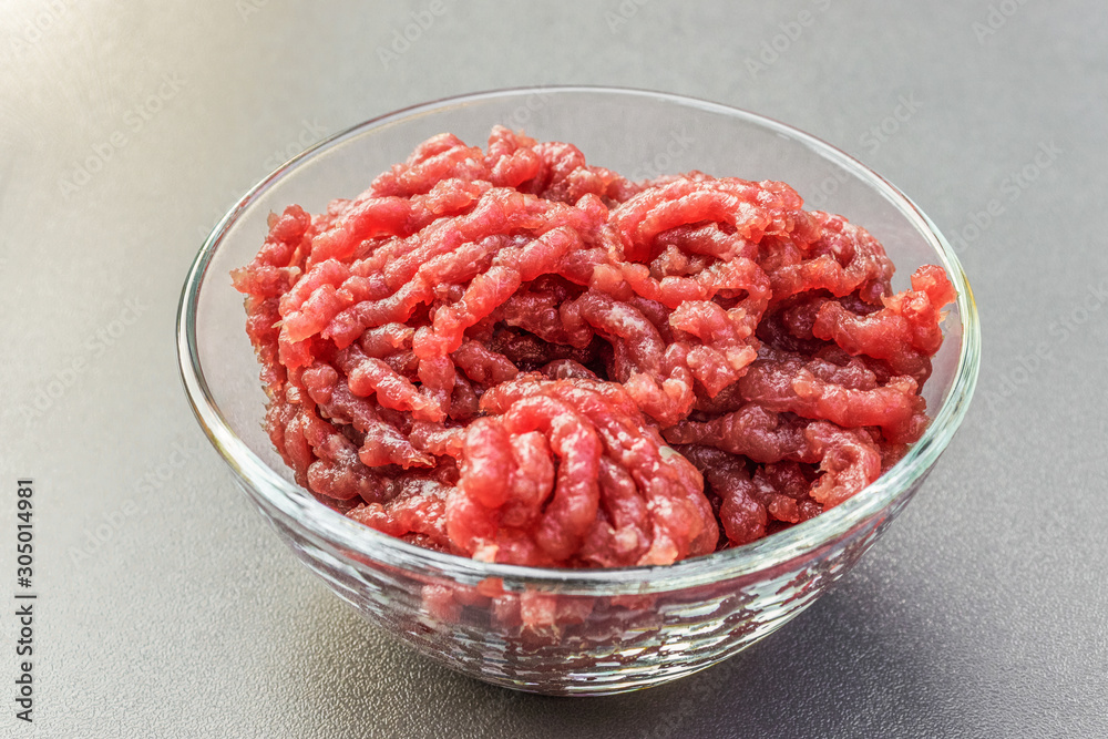 Minced beef meat in a deep transparent glass bowl on a gray background Minced beef meat in a deep transparent glass bowl on a gray background
