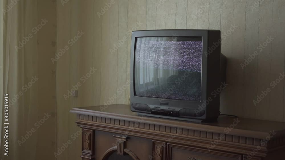 outdated black TV-set with flashing ripples stands on brown wooden drawer unit near window closeup