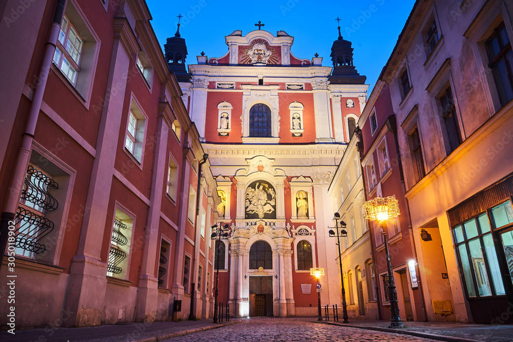 The  facade of the baroque church and the cobbled street at night in Poznan.