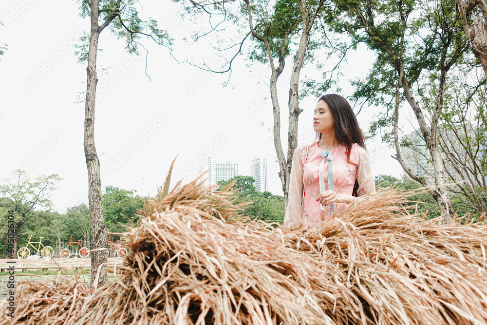Portrait of Asian women in pink dress standing behind stacked straw Portrait of Asian women in pink dress standing behind stacked straw