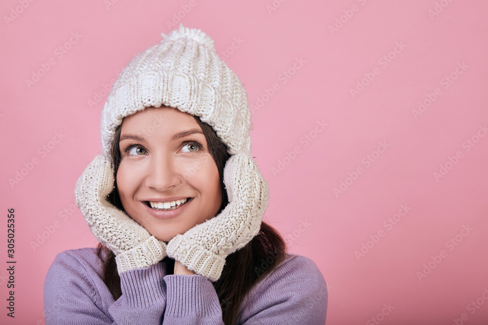 A beautiful brown-haired woman with green eyes in knitted hat holds her hands under her chin A beautiful brown-haired woman with green eyes in knitted hat holds her hands under her chin