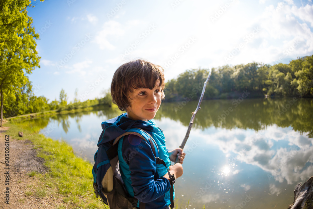 A boy with a backpack sits on the lake with a wooden stick. A boy with a backpack sits on the lake with a wooden stick.