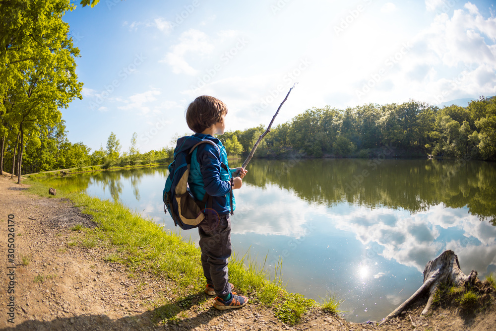 A boy with a backpack sits on the lake with a wooden stick. A boy with a backpack sits on the lake with a wooden stick.