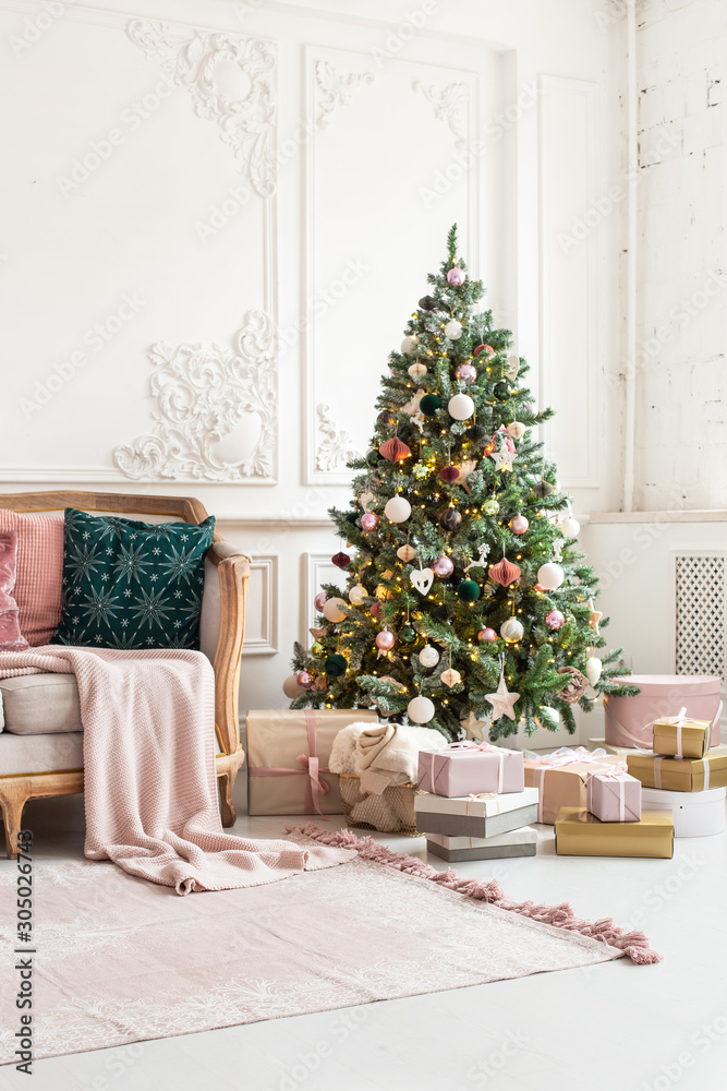 Christmas tree decorated by garland and gift boxes stands close to sofa Christmas tree decorated by garland and gift boxes stands close to sofa