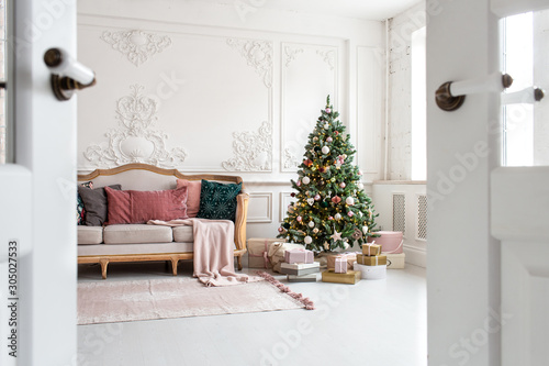 White sofa standing next to christmas tree surrounded by gift boxes. Selective focus